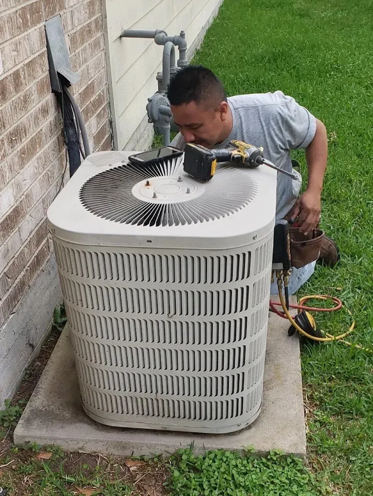 Technician inspecting an outdoor air conditioning unit near a house.